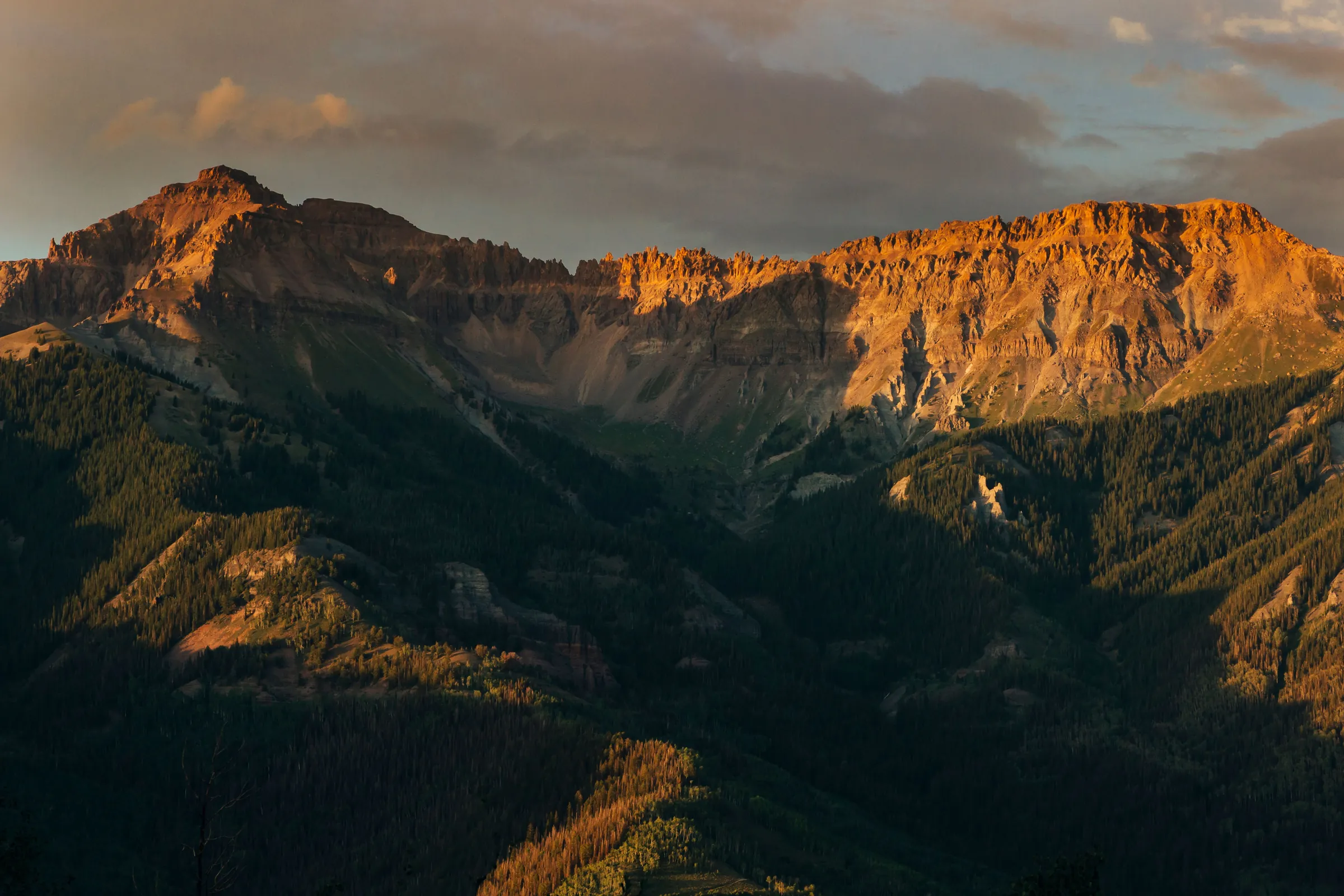 Alpenglow lighting a jagged San Juan Mountains ridge above a forested valley